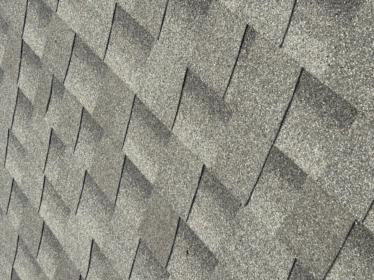 Close-up view of asphalt shingles showing multiple impact marks and indentations consistent with hail damage across the