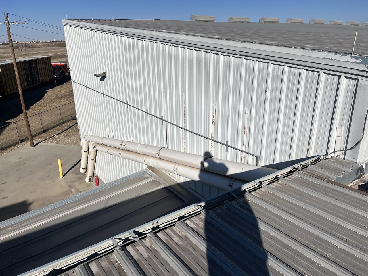 A white corrugated metal panel wall and roof section of a commercial building with visible pipe jacks and roof vents along