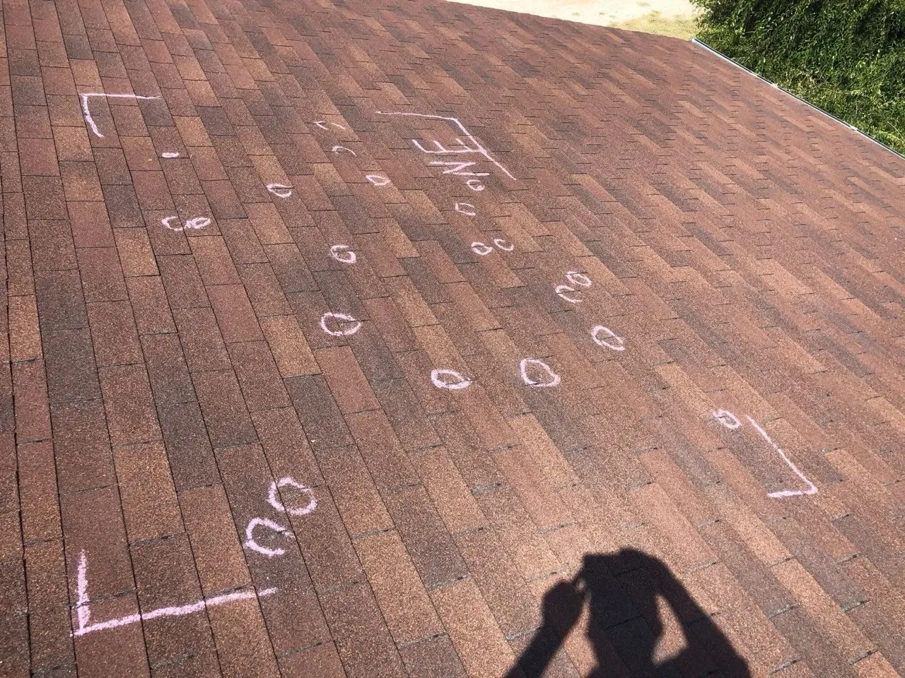 Hail impact points circled with white chalk on a residential shingle roof — documentation packet prepared for insurance adjuster review