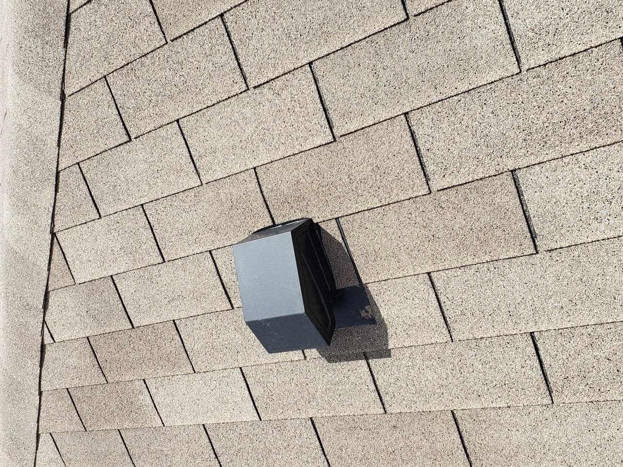 Close-up of a plastic turtle vent installed on beige asphalt shingles — a common alternative to continuous ridge venting