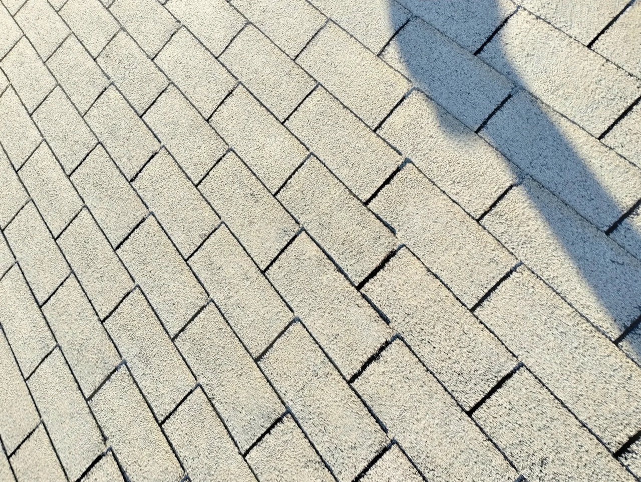 Close-up view of light-colored asphalt shingles arranged in a herringbone or diagonal pattern on a residential roof