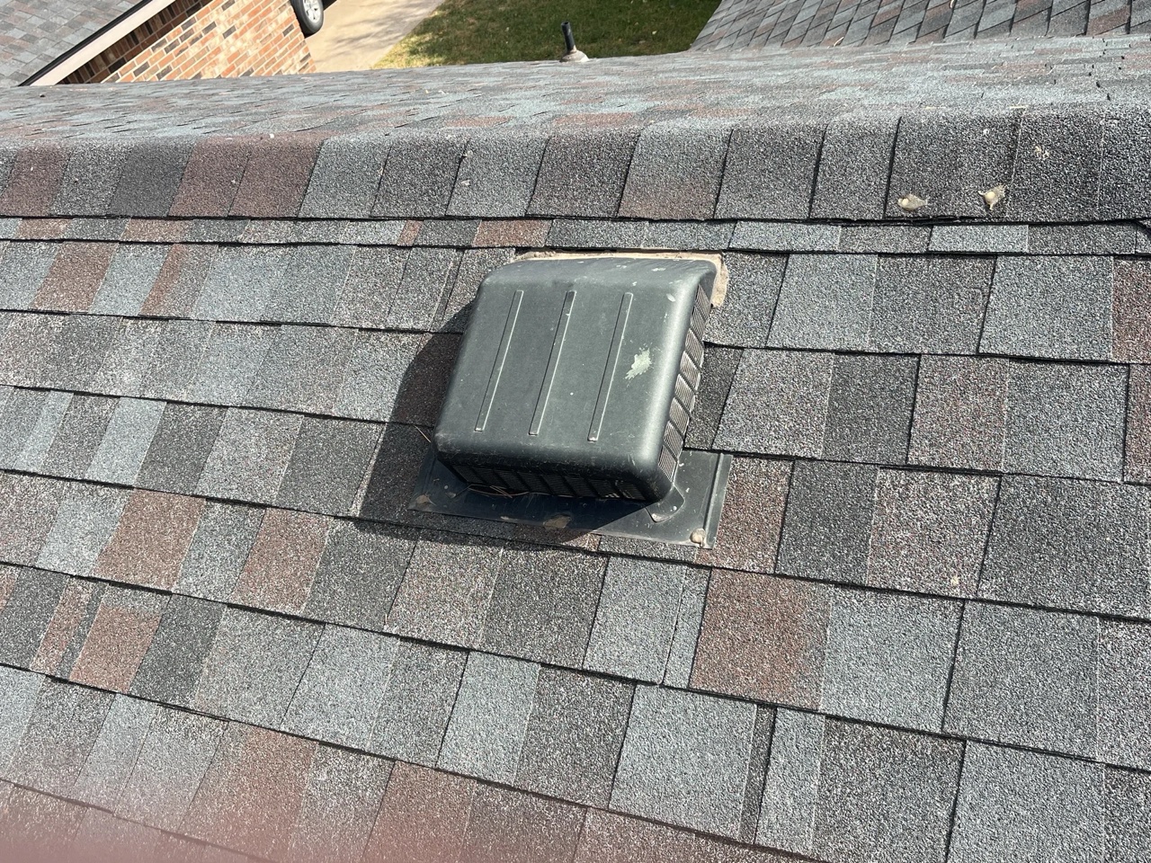 A black plastic turtle vent installed on a gray asphalt shingle roof, showing the static ventilation component used for