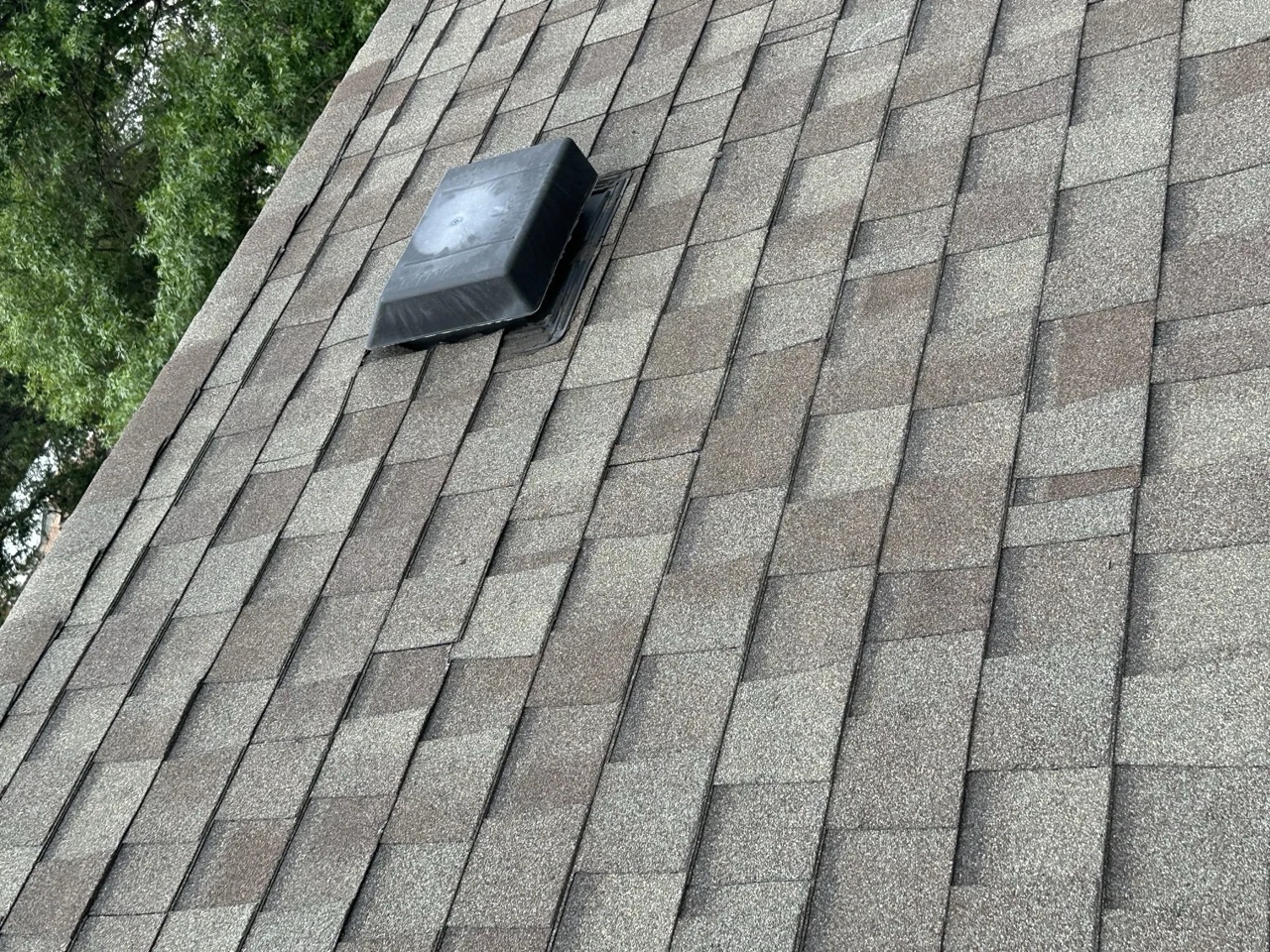 A turtle vent installed on a gray asphalt shingle roof showing the field installation of shingles and penetration flashing